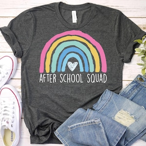 May include: A dark gray t-shirt with a rainbow and a heart design. The text "After School Squad" is printed below the rainbow.