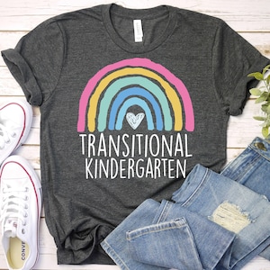 May include: A dark gray t-shirt with a rainbow and heart design. The text "Transitional Kindergarten" is printed below the rainbow.