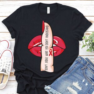 May include: Black t-shirt with a red lip and a finger over the mouth, with the text "Don't judge what you don't understand" and a red ribbon.