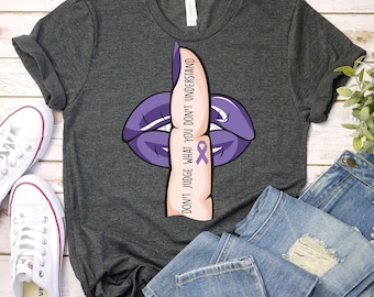 May include: A dark gray t-shirt with a purple lips design and a finger over the lips. The finger has a purple ribbon on it and the text "Don't judge what you don't understand".
