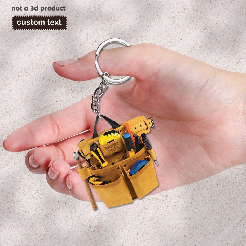 May include: A miniature tool belt keychain with a brown leather strap, multiple pockets, and various tools. The keychain is personalized with the name "HARRY" and the year "2023".