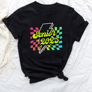May include: Black t-shirt with a rainbow checkered design and a lightning bolt graphic. The text "Senior 2025" is written in yellow with a retro font.