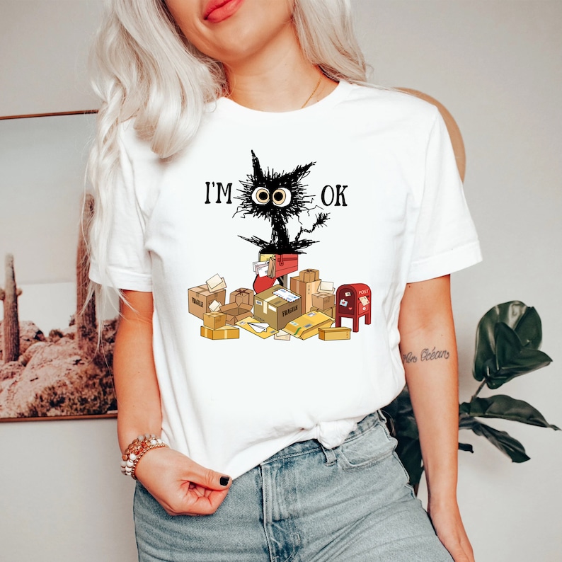May include: White t-shirt with a black cat illustration and the text "I'M OK". The cat is surrounded by packages and mailboxes.