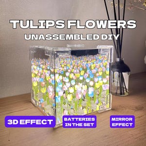 以下が含まれることがあります： 鏡が内側にあり、3D効果を生み出す透明なアクリルキューブ。キューブはカラフルなプラスチック製のチューリップでいっぱい。画像の上部には「TULIPS FLOWERS UNASSEMBLED DIY」というテキストがあります。左下には「3D EFFECT」、中央下には「BATTERIES IN THE SET」、右下には「MIRROR EFFECT」というテキストがあります。