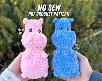 May include: Two crocheted hippopotamus amigurumi toys, one pink and one blue. The toys are made with a fluffy yarn and have black eyes. The text "NO SEW PDF CROCHET PATTERN" is displayed above the toys.