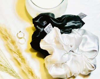 May include: Two satin scrunchies, one black and one white. The white scrunchie is in focus and has a small label with the text "LR" and "Made in China".