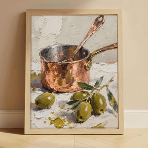 May include: Oil painting of a copper saucepan with a spoon inside, set on a white surface with green olives and olive branches. The artwork is framed in a light wood frame, with a neutral background.