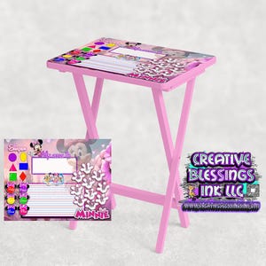 Puede incluir: Mesa plegable rosa con diseño de Minnie Mouse. La superficie de la mesa tiene un personaje de Minnie Mouse y las palabras "Creative Blessings Ink LLC" están impresas en el lateral de la mesa. La mesa se acompaña de una hoja de actividades con temática de Minnie Mouse con formas, líneas y un espacio para escribir.
