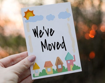May include: A white card with a blue sky and sun illustration. The card says "We've Moved" in black handwriting. There are five cartoon houses at the bottom of the card.