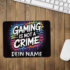 Könnte beinhalten: Schwarzes rechteckiges Mauspad mit dem Text "GAMING IS NOT A CRIME" in Weiß und Regenbogenfarben. Das Mauspad enthält auch den Text "DEIN NAME" in Weiß. Eine weiße Maus und Tastatur befinden sich im Hintergrund.