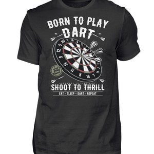 Op de afbeelding: Een zwart T-shirt met een witte afbeelding van een dartbord en pijlen. De tekst "Born to Play Dart" staat boven het dartbord en "Shoot to Thrill" staat onder het dartbord. De tekst "Eat - Sleep - Dart - Repeat" staat onder de zin "Shoot to Thrill".