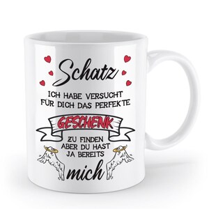 Könnte beinhalten: Weißer Keramikbecher mit Henkel, mit dem deutschen Wort "Schatz" in Schreibschrift, sowie Text und Herzgrafiken. Der Becher hat ein Design mit den Worten "ICH HABE VERSUCHT FÜR DICH DAS PERFEKTE GESCHENK ZU FINDEN ABER DU HAST JA BEREITS mich."