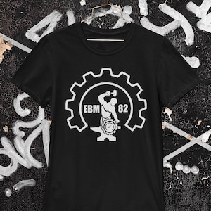 May include: Black t-shirt featuring a white graphic of a cog with a silhouette of a person holding a hammer and an anvil inside. The text "EBM 82" is within the cog.