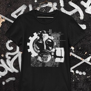 May include: Black t-shirt with a white graphic of a gas mask with a gear and a digital pattern.