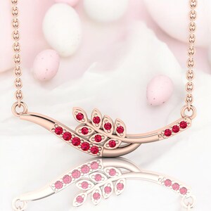 Puede incluir: Un collar de oro rosa con diseño de hoja. El collar presenta una barra curva con una serie de pequeñas piedras preciosas rojas redondas. Un grupo de piedras preciosas rojas en forma de hoja está centrado en la barra. La cadena es delicada.