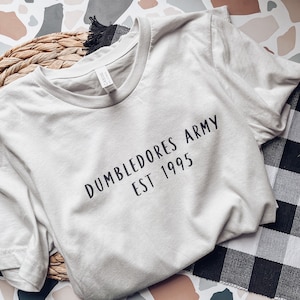 May include: A light gray t-shirt with the text "Dumbledore's Army Est 1995" printed in black.