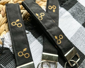 May include: Three black keychains with gold-colored glasses and lightning bolt designs. Each keychain has a silver metal ring.