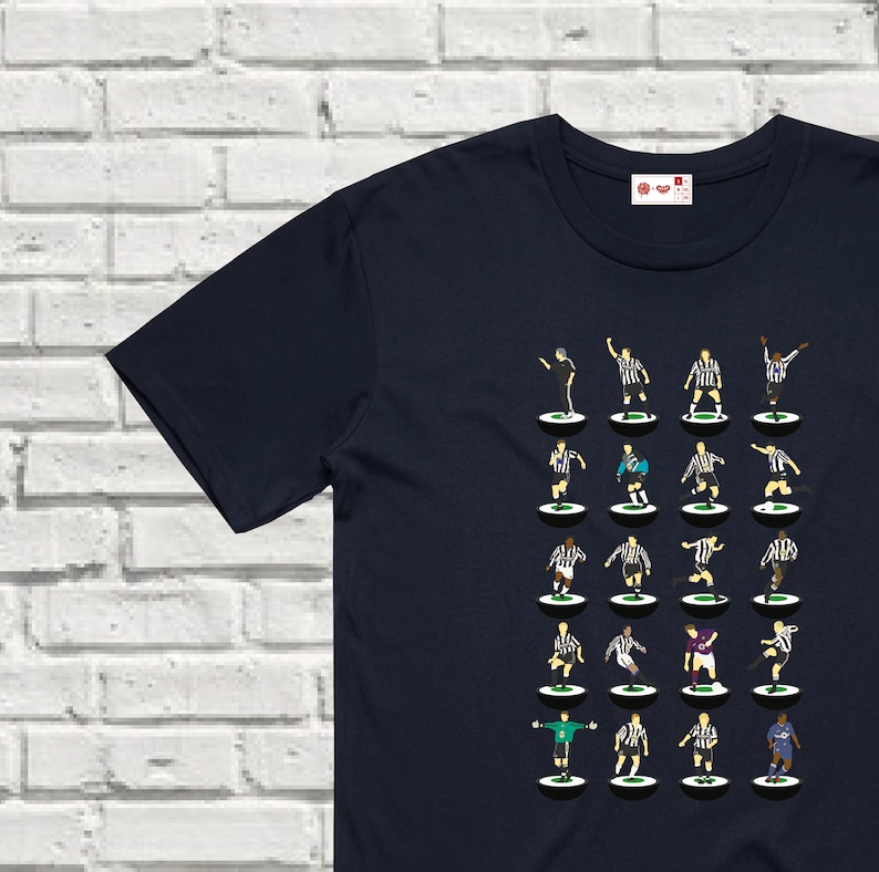 Puede incluir: Una camiseta azul marino con un dise&ntilde;o de 24 jugadores de f&uacute;tbol con uniformes blanco y negro sobre un fondo blanco. Los jugadores est&aacute;n dispuestos en cuatro filas de seis jugadores cada una.