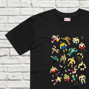 Könnte beinhalten: Schwarzes T-Shirt mit einem Grafikdruck von verschiedenen Wrestlern in verschiedenen Posen. Die Wrestler sind alle im Cartoon-Stil gehalten und tragen farbenfrohe Outfits.