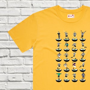 Puede incluir: Una camiseta amarilla con una ilustraci&oacute;n en blanco y negro de un equipo de f&uacute;tbol. Los jugadores est&aacute;n representados en un estilo retro, de pie sobre peque&ntilde;os c&iacute;rculos.