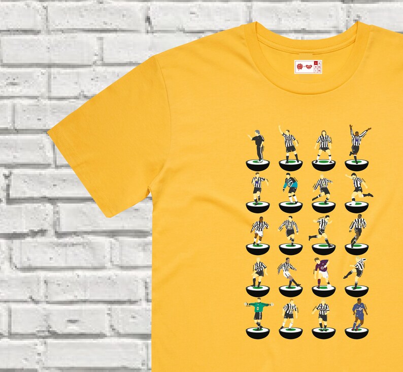 Puede incluir: Una camiseta amarilla con una ilustraci&oacute;n en blanco y negro de un equipo de f&uacute;tbol. Los jugadores est&aacute;n representados en un estilo retro, de pie sobre peque&ntilde;os c&iacute;rculos.
