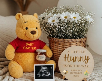 May include: A plush yellow bear wearing a red shirt with the text BABY CARTER, a small honey jar labeled SEPTEMBER 2026, an ultrasound scan, and a round wooden sign reading A LITTLE HUNNY IS ON THE WAY ARRIVING SEPTEMBER 2026.