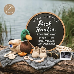 May include: A baby announcement sign with a black chalkboard background and a wooden frame. The sign reads "Our Little Duck Hunter is on the way Baby Williams September 2025". There is a stuffed duck, baby booties, a pair of binoculars, and a sonogram photo on a wooden surface.