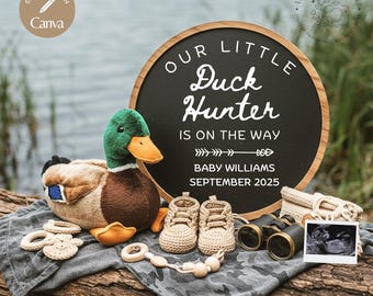May include: A baby announcement sign with a black chalkboard background and a wooden frame. The sign reads "Our Little Duck Hunter is on the way Baby Williams September 2025". There is a stuffed duck, baby booties, a pair of binoculars, and a sonogram photo on a wooden surface.