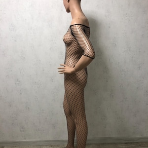 May include: A black fishnet bodysuit on a mannequin. The off-the-shoulder garment features a diamond-shaped mesh design, covering the torso and legs. The mannequin is positioned in profile, showcasing the bodysuit's form-fitting silhouette.