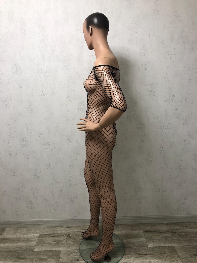 May include: A black fishnet bodysuit on a mannequin. The off-the-shoulder garment features a diamond-shaped mesh design, covering the torso and legs. The mannequin is positioned in profile, showcasing the bodysuit's form-fitting silhouette.