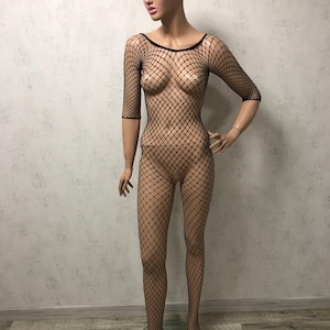 May include: A black fishnet bodysuit on a mannequin. The bodysuit features a diamond-shaped net pattern, a round neckline, and three-quarter sleeves. The mannequin is standing on a clear, circular base.