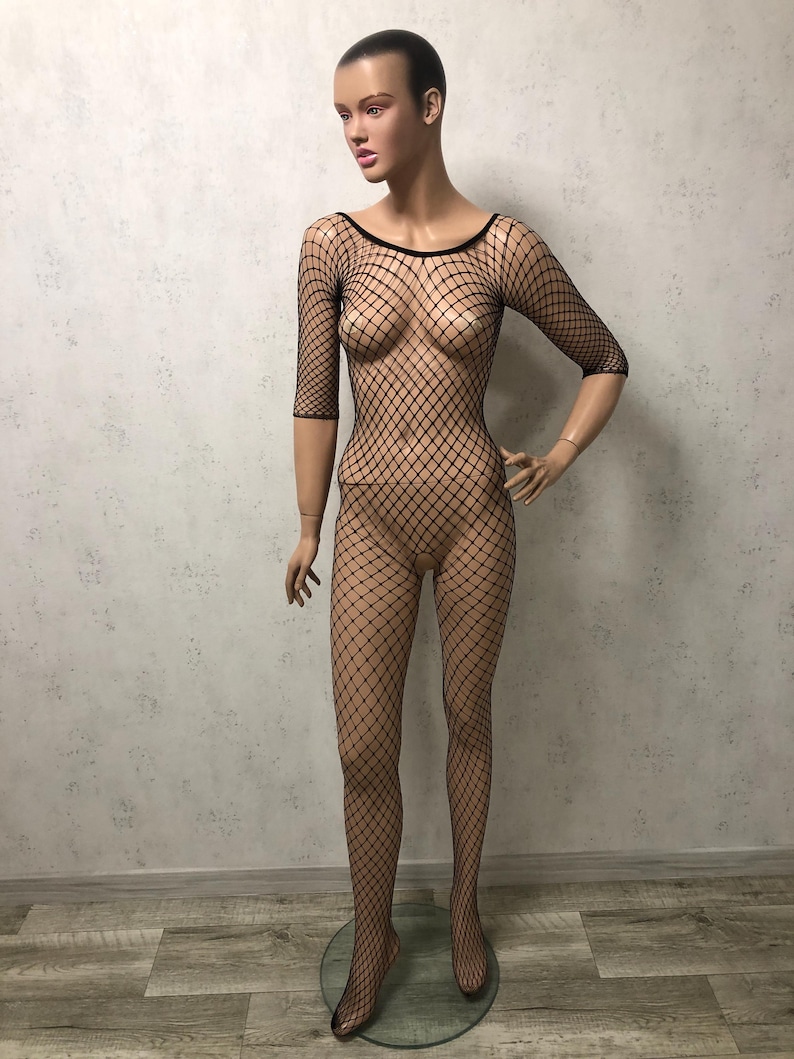 May include: A black fishnet bodysuit on a mannequin. The bodysuit features a diamond-shaped net pattern, a round neckline, and three-quarter sleeves. The mannequin is standing on a clear, circular base.