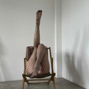 Pu&ograve; includere: Una persona con calze a rete nere &egrave; seduta su una sedia pieghevole di legno con le gambe incrociate.