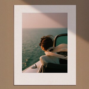 Puede incluir: Fotografía enmarcada de una persona mirando al océano desde un barco. La persona lleva gafas de sol y una bufanda. El cielo es de un rosa suave y el agua es de un azul verdoso profundo.