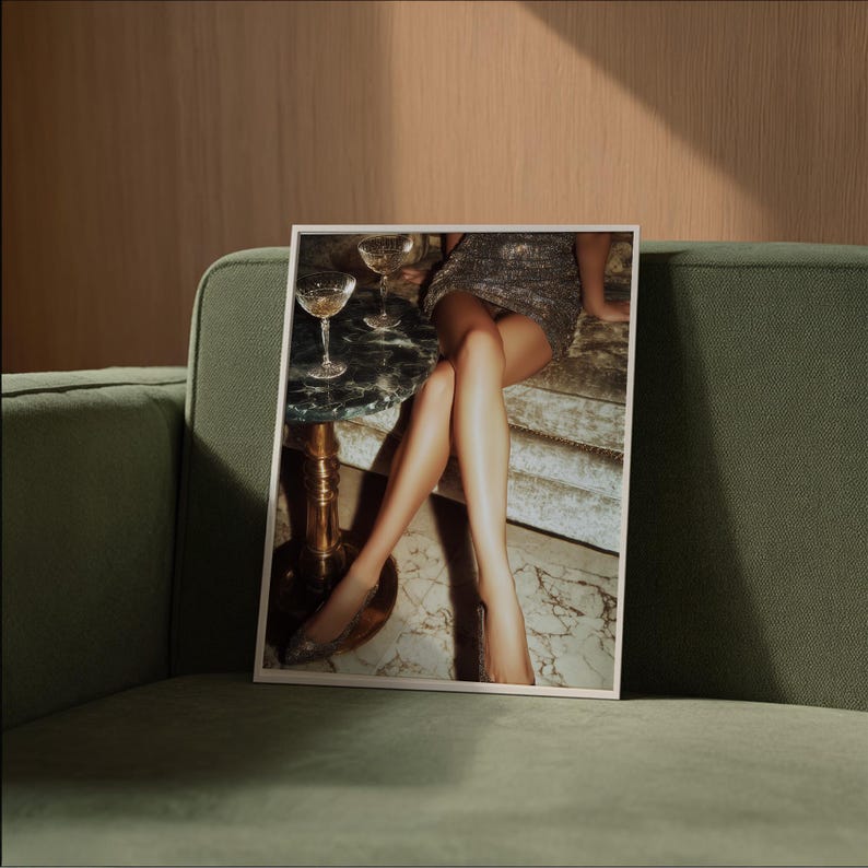 Puede incluir: Una impresi&oacute;n enmarcada que presenta una escena glamurosa con una mujer con un vestido brillante, copas de champ&aacute;n y una peque&ntilde;a mesa. La imagen est&aacute; ambientada sobre un sof&aacute; verde y una pared de madera, creando un ambiente lujoso.