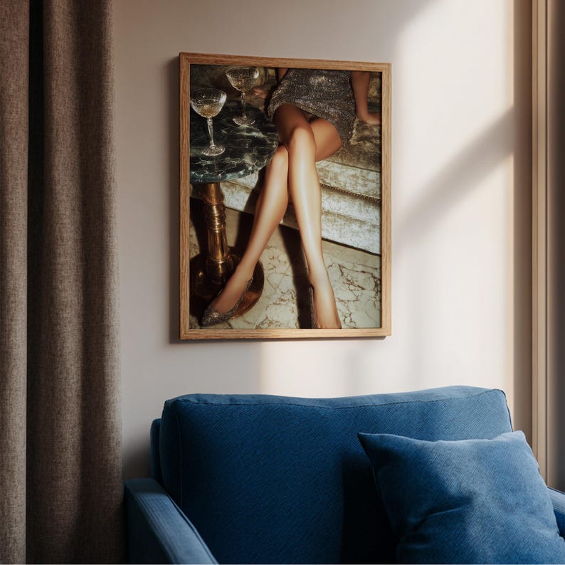 Puede incluir: Una impresi&oacute;n enmarcada que presenta una escena glamurosa. La imagen muestra a una mujer con un vestido plateado con lentejuelas, sentada cerca de una peque&ntilde;a mesa con dos copas de champ&aacute;n. La atenci&oacute;n se centra en las piernas de la mujer y el entorno elegante.