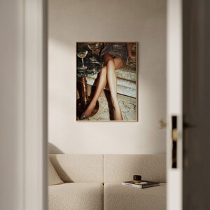 Puede incluir: Impresi&oacute;n art&iacute;stica enmarcada que presenta una escena glamurosa. La obra de arte representa las piernas de una persona y un vestido brillante, con copas de champ&aacute;n sobre una peque&ntilde;a mesa. La impresi&oacute;n est&aacute; en un marco dorado, a&ntilde;adiendo un toque de elegancia.