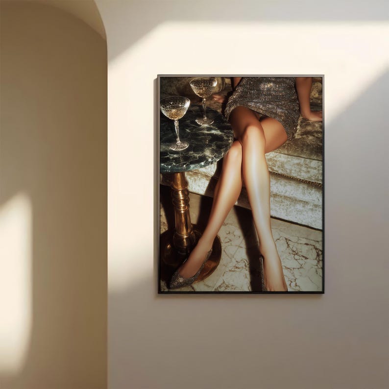 Puede incluir: Impresi&oacute;n enmarcada que representa una escena glamurosa con dos copas de champ&aacute;n sobre una mesa peque&ntilde;a. La mesa tiene una tapa de m&aacute;rmol y una base dorada. La imagen tambi&eacute;n muestra a una persona con un vestido de lentejuelas y tacones brillantes.