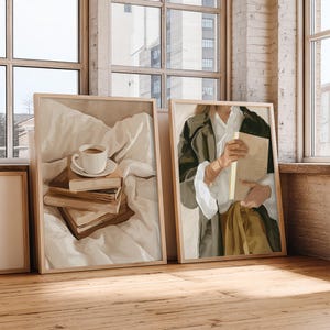 May include: Two framed art prints. One features a coffee cup on a stack of books, the other depicts a person holding a book. Both are in neutral tones with wooden frames, set against a window.