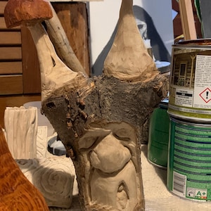 Puede incluir: Una escultura de madera caprichosa de una cara con una nariz grande y una boca pequeña, tallada en un tronco de árbol. Dos tapas en forma de hongo con tapas de color marrón rojizo se extienden desde la parte superior del tronco. Una obra de arte única.