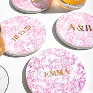 Posavasos redondos de 10 cm con monograma floral personalizado, rosa y blanco, con letras doradas, nombre y fecha, ideal como regalo de boda.