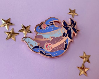 Op de afbeelding: Een rozégouden theepot emaille pin met een blauw en wit hemels ontwerp. De theepot heeft een stervormig handvat en een strik op de tuit. De pin is omgeven door gouden stervormige versieringen.