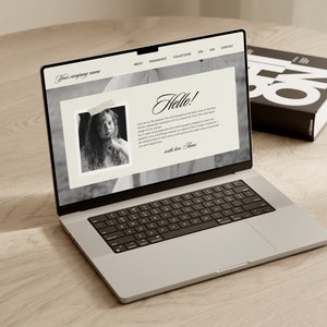May include: A laptop computer open to a website with the text "Hello!" and a black and white photo of a young girl. The website also includes the text "Your company name" and navigation links for "About", "Engagement", "Collections", "Blog", "FAQ", and "Contact".