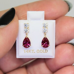 May include: A pair of 14kt gold earrings with a pear-shaped ruby gemstone and a row of clear cubic zirconia stones.
