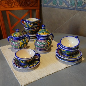 May include: A blue and yellow ceramic tea set with a teapot, sugar bowl, creamer, and two cups and saucers. The set is decorated with intricate floral patterns.