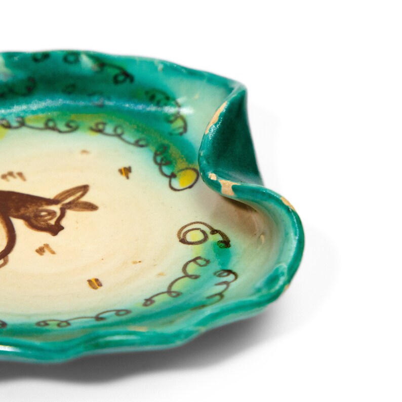 Puede incluir: Un plato de cer&aacute;mica verde con interior blanco y un dise&ntilde;o de toro pintado en marr&oacute;n. El plato tiene un borde ondulado y est&aacute; decorado con espirales verdes y amarillas.