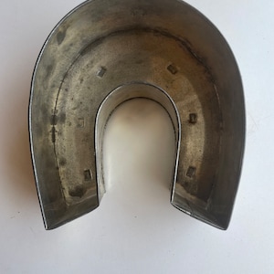 May include: A silver metal horseshoe-shaped cake pan. The pan has a smooth, slightly worn surface and is designed to create a ring-shaped cake.