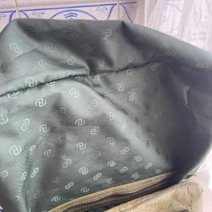 May include: Inside view of a green leather handbag. The lining is a darker green fabric with a repeating pattern of a stylized letter "R". The zip is visible at the bottom of the bag.