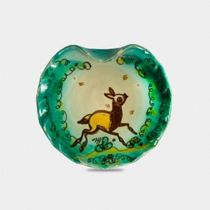 Puede incluir: Un peque&ntilde;o plato de cer&aacute;mica verde con interior blanco y un dise&ntilde;o pintado de un ciervo amarillo y marr&oacute;n corriendo a trav&eacute;s de un patr&oacute;n de enredaderas verdes.