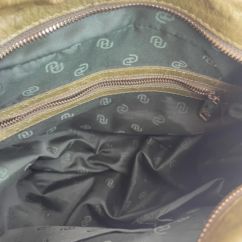 May include: Olive green leather handbag with a zip closure. The interior is dark green with a repeating pattern. The bag has a textured exterior and a metallic zip.